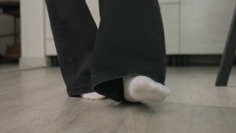 close up of two adults legs walking away from door frame one barefoot other wearing sock and holding handbag on wood floor capturing motion and transition from home interior to corridor