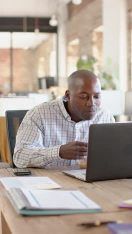 vertical video of african american casual businessman using laptop and having lunch, slow motion