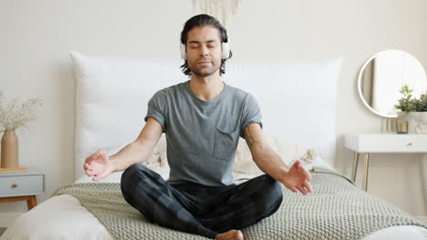 man meditating and listening to music in bed
