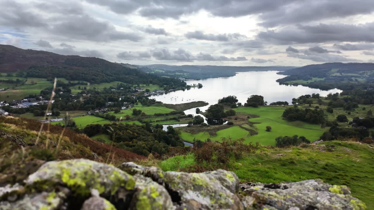 Moving over rocks on a hilltop to reveal Lake Windermere in the distance. Lake District, UK