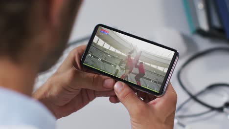 Composite-of-male-doctor-watching-rugby-match-on-smartphone