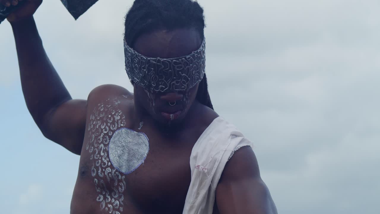 The tropical beach serves as the backdrop for a muscular, dark-skinned man perfectly in character as Nekharis cosplay