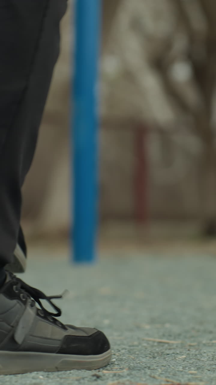 Close-up of a person s legs jogging quickly, wearing black jeans and black sneakers, with a blurred view of blue iron bars in the background