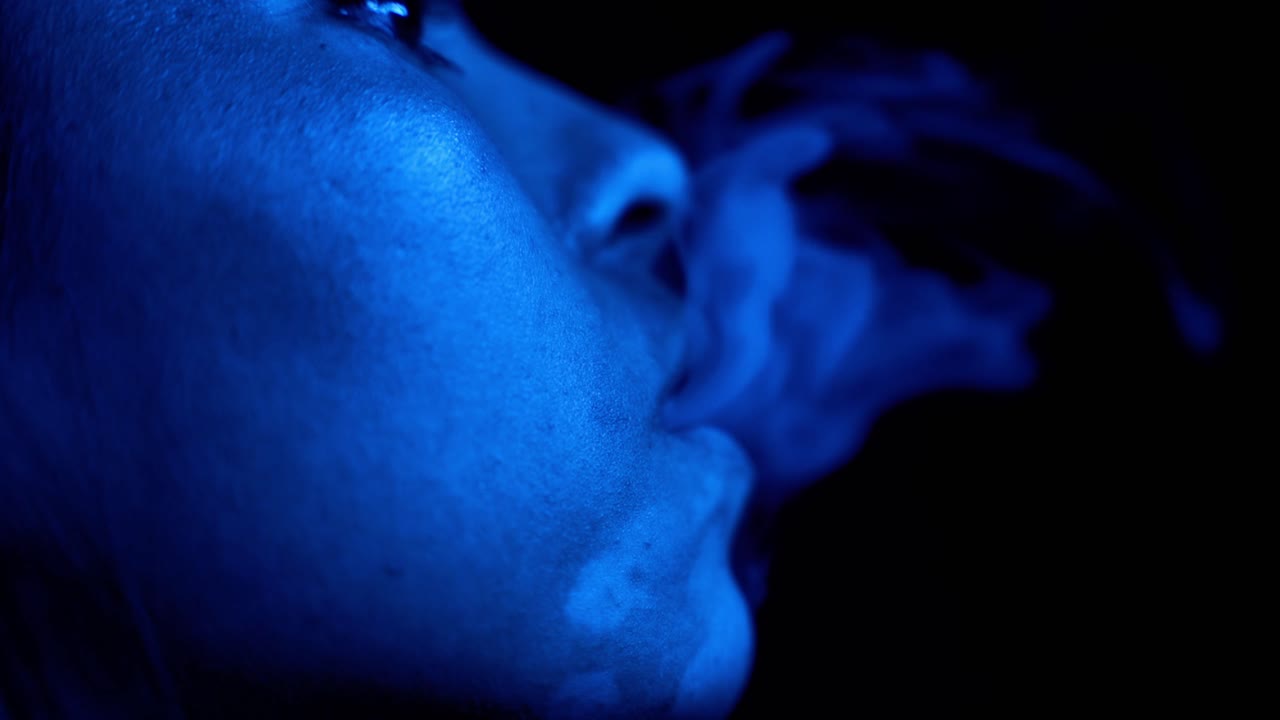 Woman smoke in blue light, close up face and lips view