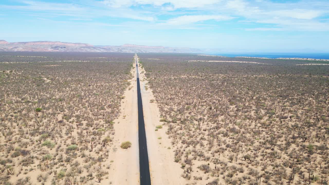 Long stretch of road through a desert landscape near La Paz, Mexico, with coastline visible
