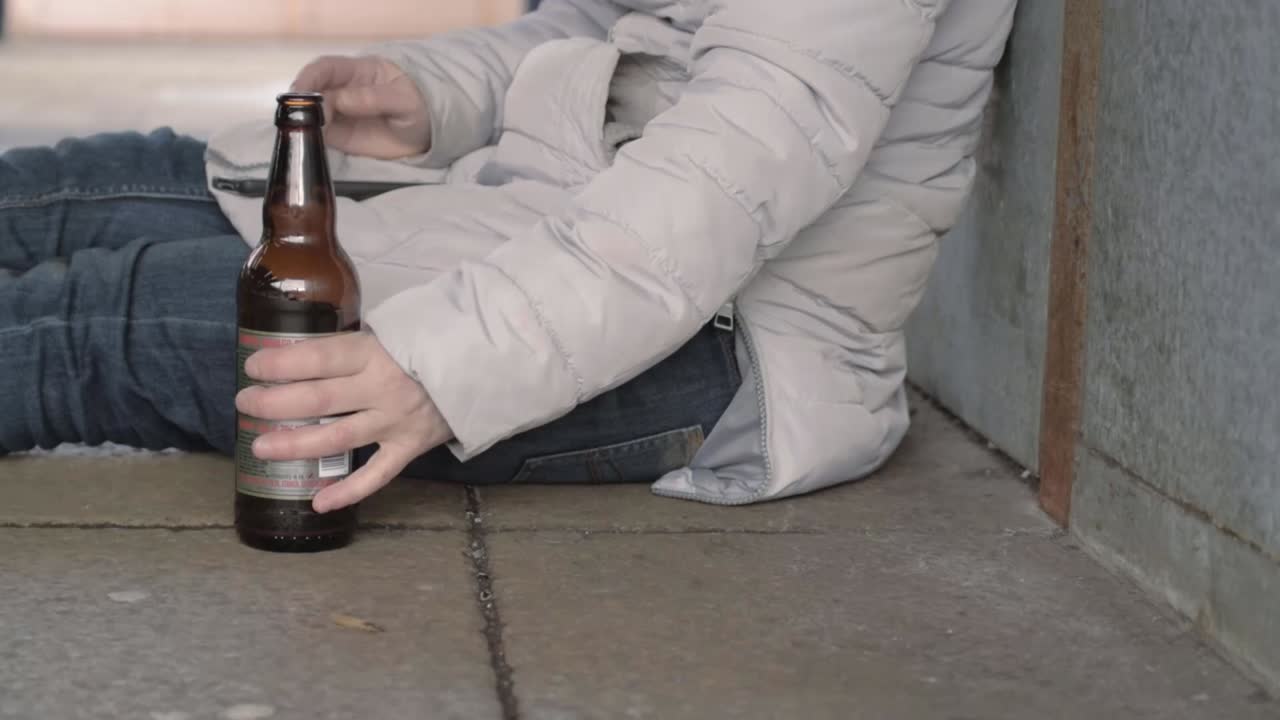 Woman sitting in urban scene drinking beer from bottle using mobile phone