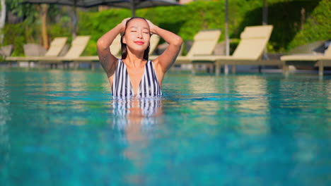 Sexy-Junge-Frau-Streichelt-Ihr-Nasses-Haar-Im-Pool-Und-Schaut-In-Die-Kamera