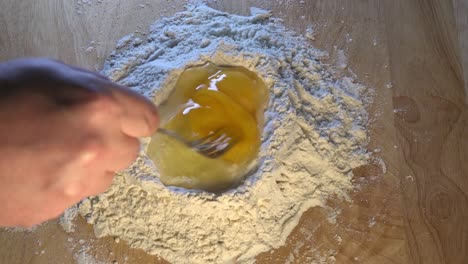 two eggs being mixed into flour on a wooden work surface for baking