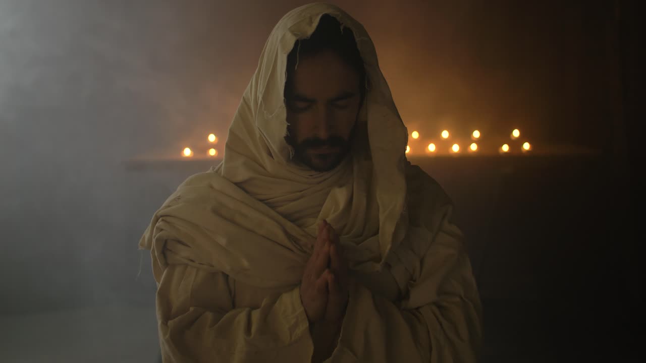 Closeup of Jesus Christ in ambient light Praying with Folded Hands with candlelight behind him for Christianity stock footage