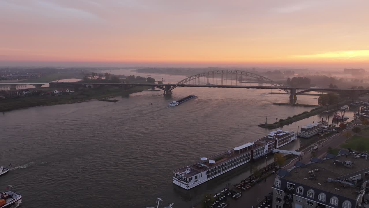 Droneopptak av et skip som seiler forbi Waalbrug med Nijmegen-skyline