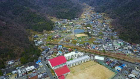 vista aérea de la ciudad de hinase, okayama, japón: impresionante toma de arriba hacia abajo de la escuela y el campo, panorámica para mostrar una ciudad encantadora con pequeños edificios, montañas verdes, cielo blanco