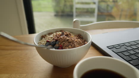 Gut-Beleuchtete-Müslischüssel-In-Der-Mittagspause-Mit-Kaffee-Und-Laptop-Auf-Einem-Holztisch