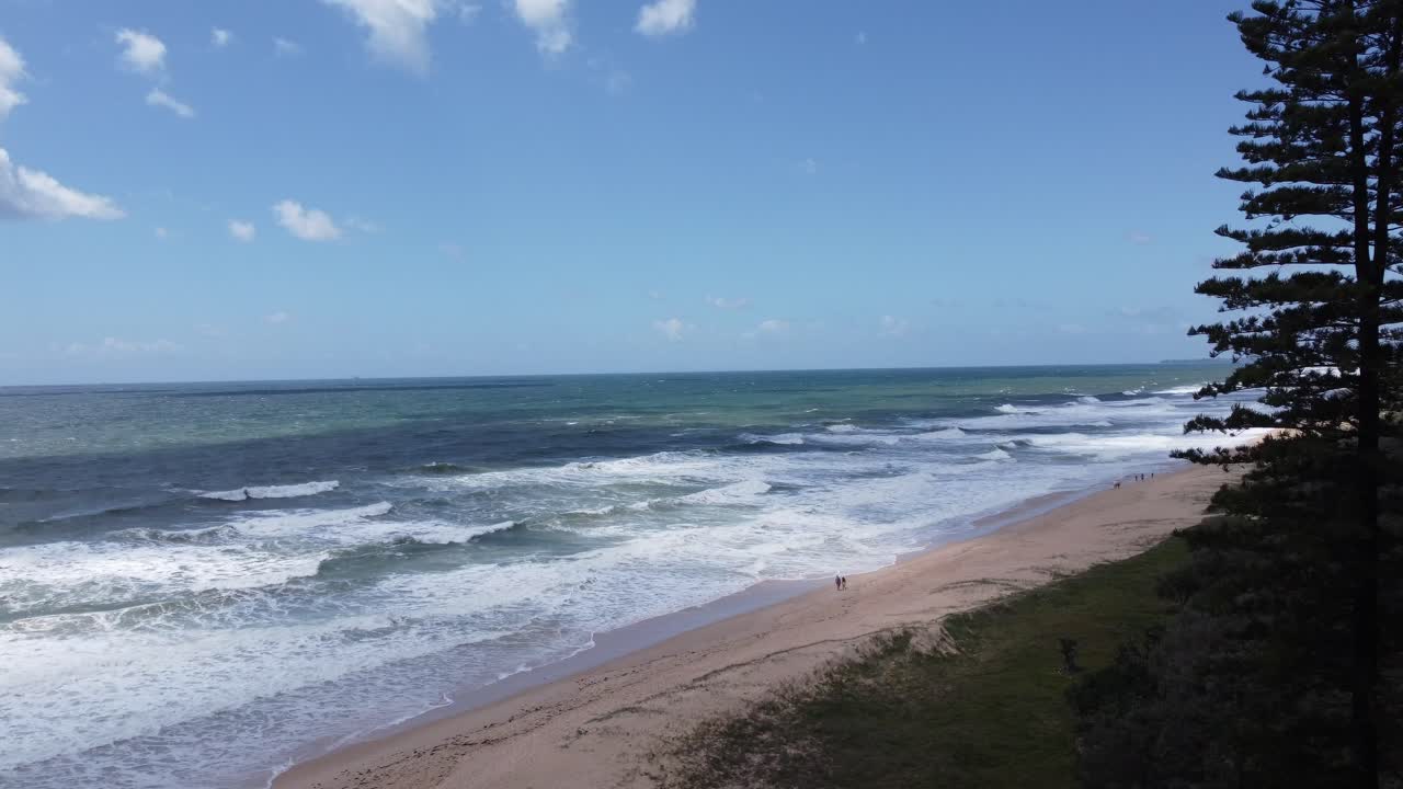 Sweeping view of a beautiful sandy beach with large crushing waves on Australia's Sunshine Coast