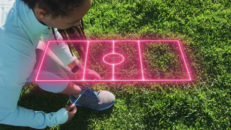 Neon-soccer-field-layout-icon-spinning-against-african-american-fit-woman-tying-her-shoe-laces