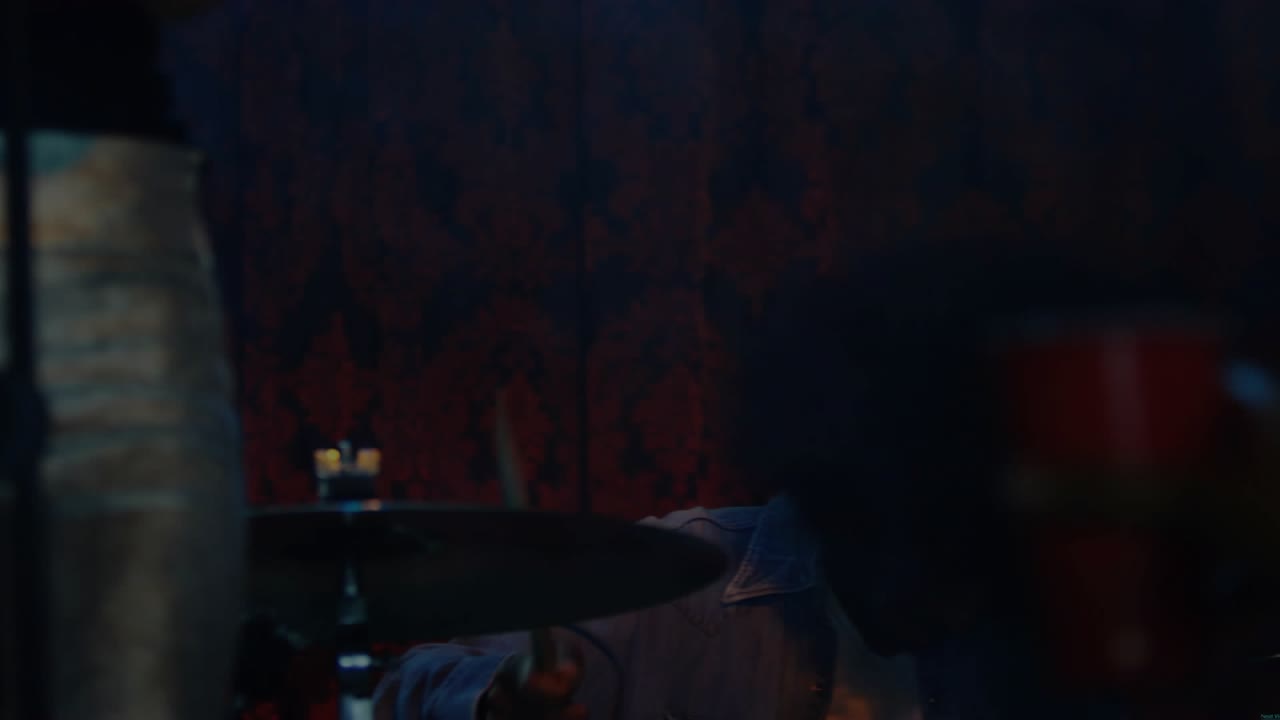 Male drummer lifting sticks, striking cymbals, toms, making music while lights revealing face