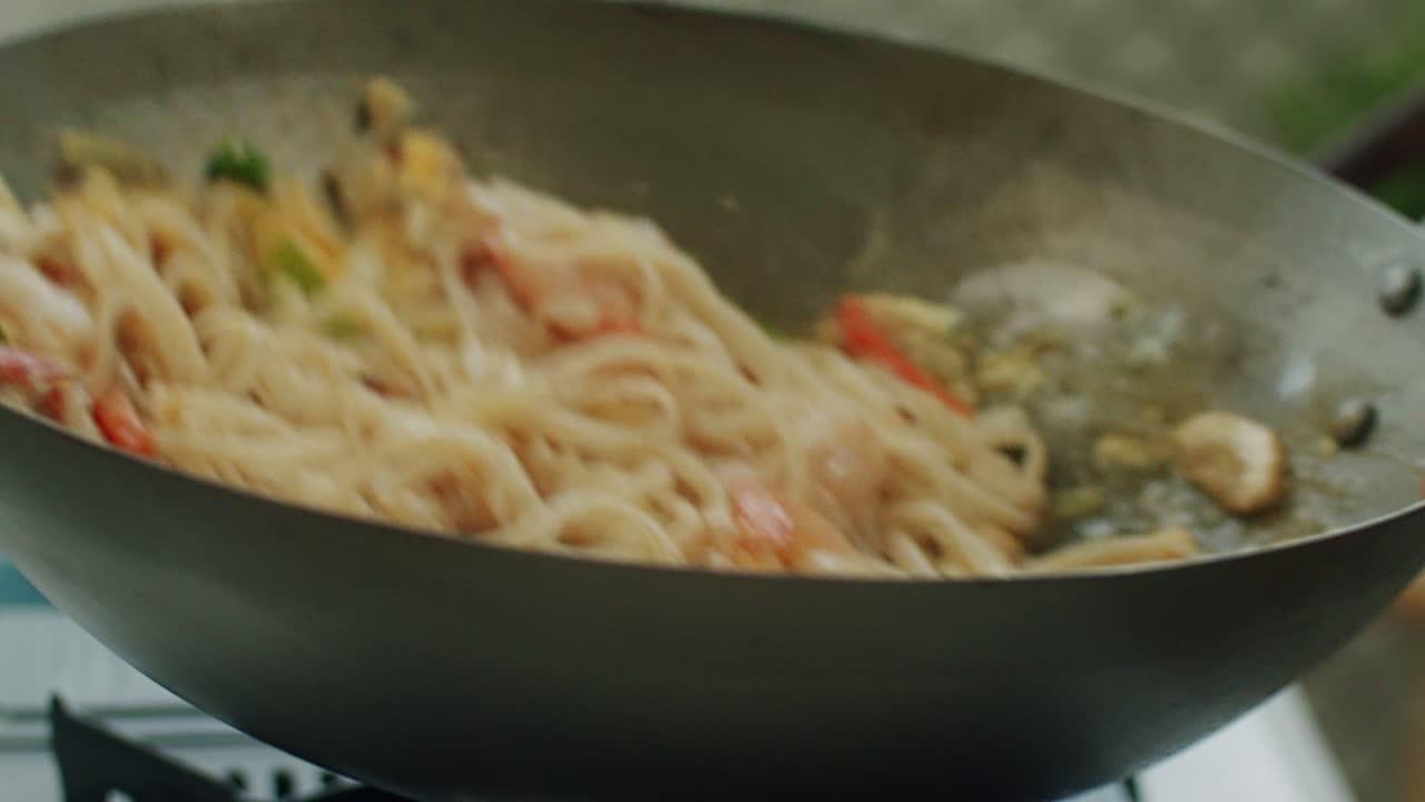 Woman stirring broth in pan with wok noodles