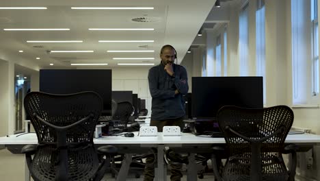 Comerciante-De-Mercado-Masculino-Dentro-De-Una-Oficina-Vacía-Mirando-Dos-Monitores-Mientras-Habla-Con-Auriculares