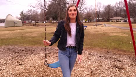 4k footage of a beautiful, young, brunette college teenager standing next to a swing set in a city park talking and laughing