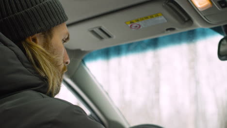 Primer-Plano-De-Un-Hombre-Barbudo-Con-Ropa-De-Invierno-Sentado-En-Su-Coche