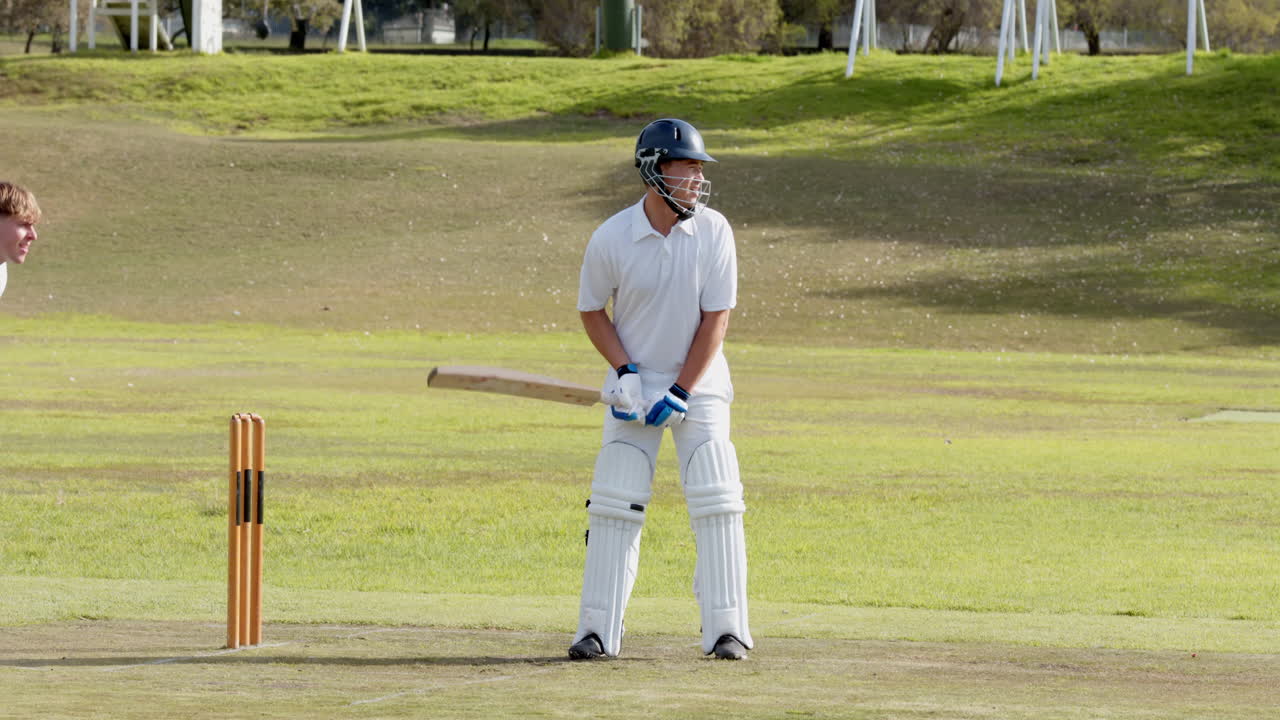 Two teams of male cricket players playing cricket, batter hitting ball with bat on pitch