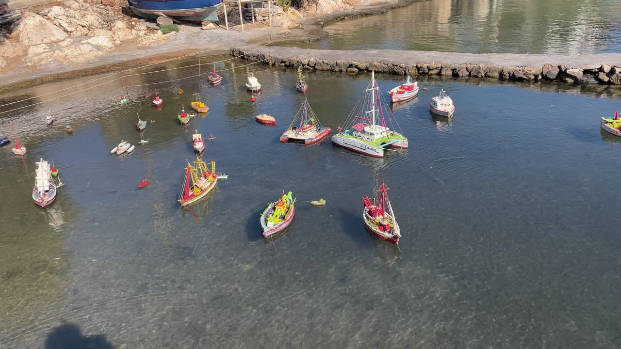 Greece,Arki Island,Model ships swinging slowly on a natural sea pond, footage moves from left to right. some real size fisherman's boats behind the pond and a fisherman's boat on land under trees.