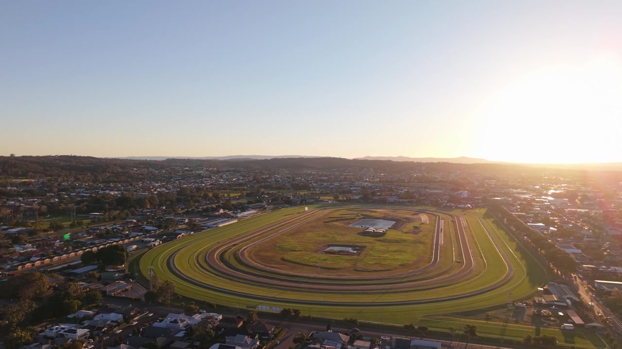 Newcastle Væddeløbsbane i New South Wales omgivet af forstæder under varmt solnedgangslys, luftfoto med etablerende tilbagetrækning