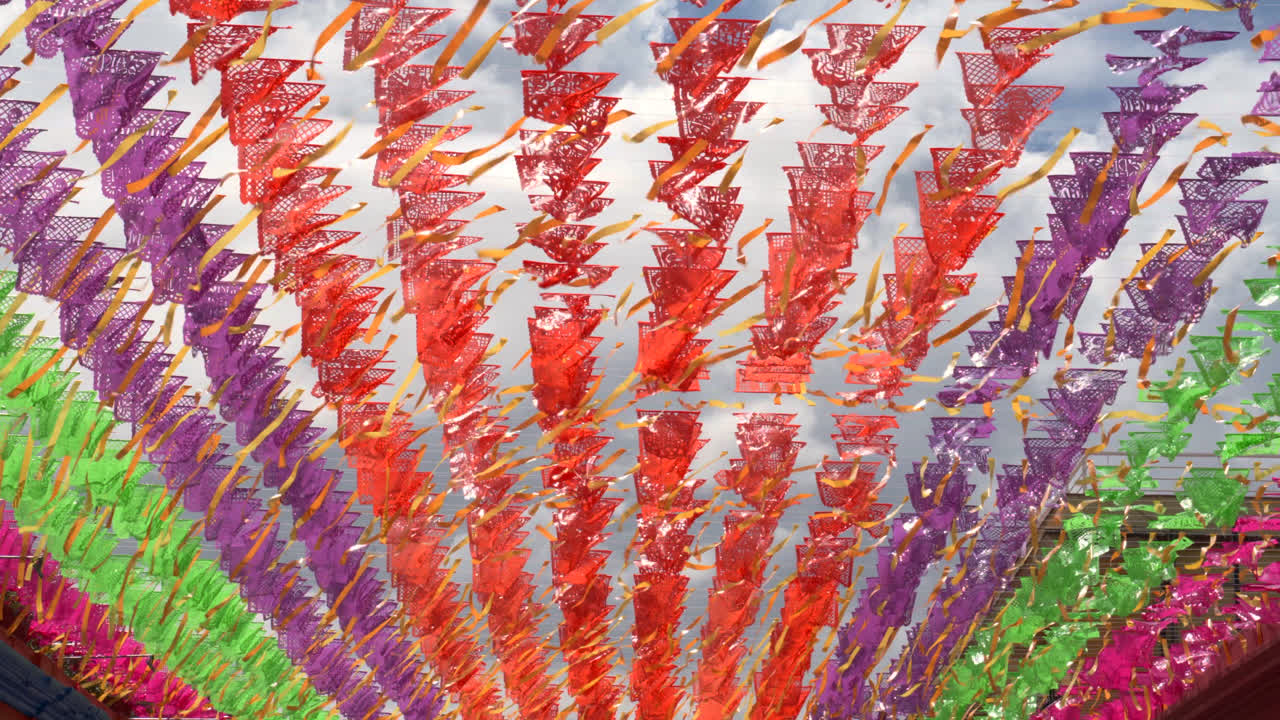 Papel picado rows sway across open market walkway creating colorful patterned canopy overhead, textured beautiful backdrop