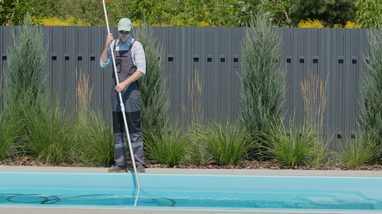 trabajador en monos aspirando la piscina en el patio trasero de la casa