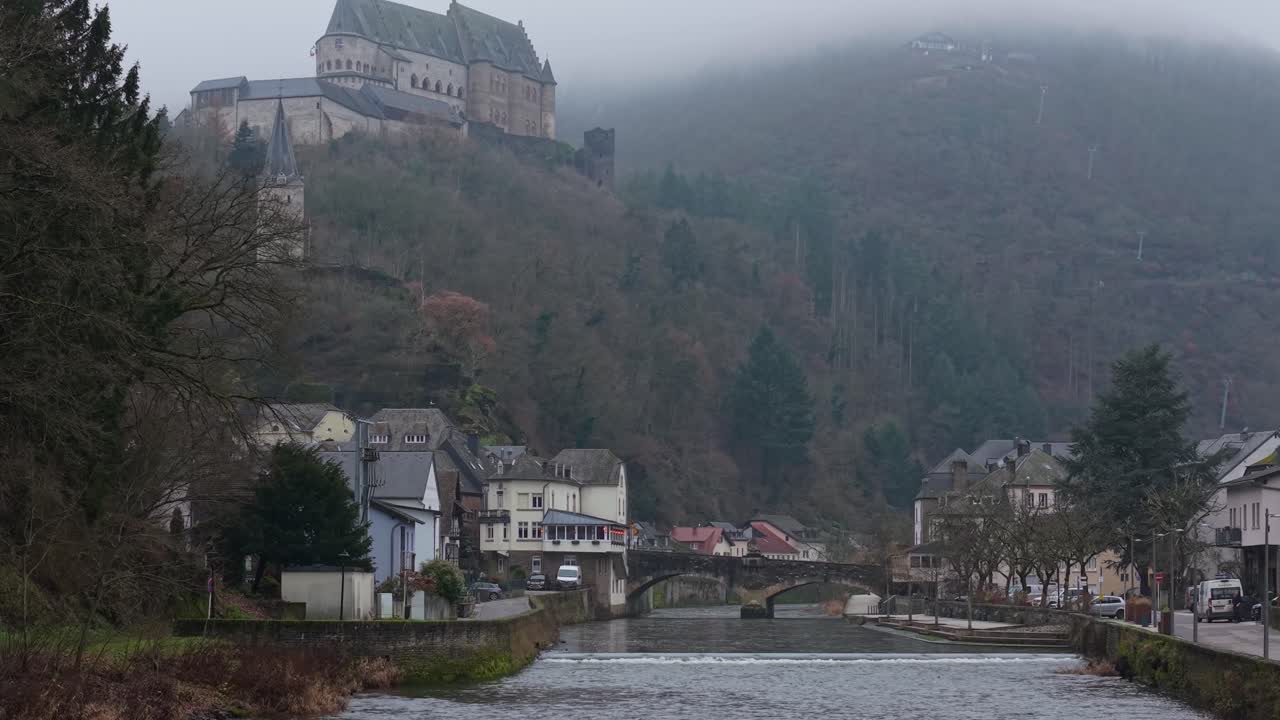 Riprese con drone sul fiume Vianden che catturano il villaggio mentre il castello emerge sulla cima della collina attraverso la nebbia invernale, creando una scena stagionale calma e suggestiva.