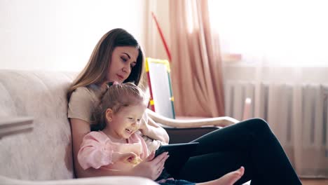 Travelling-Young-mother-and-sweet-daughter-are-sitting-on-the-couch