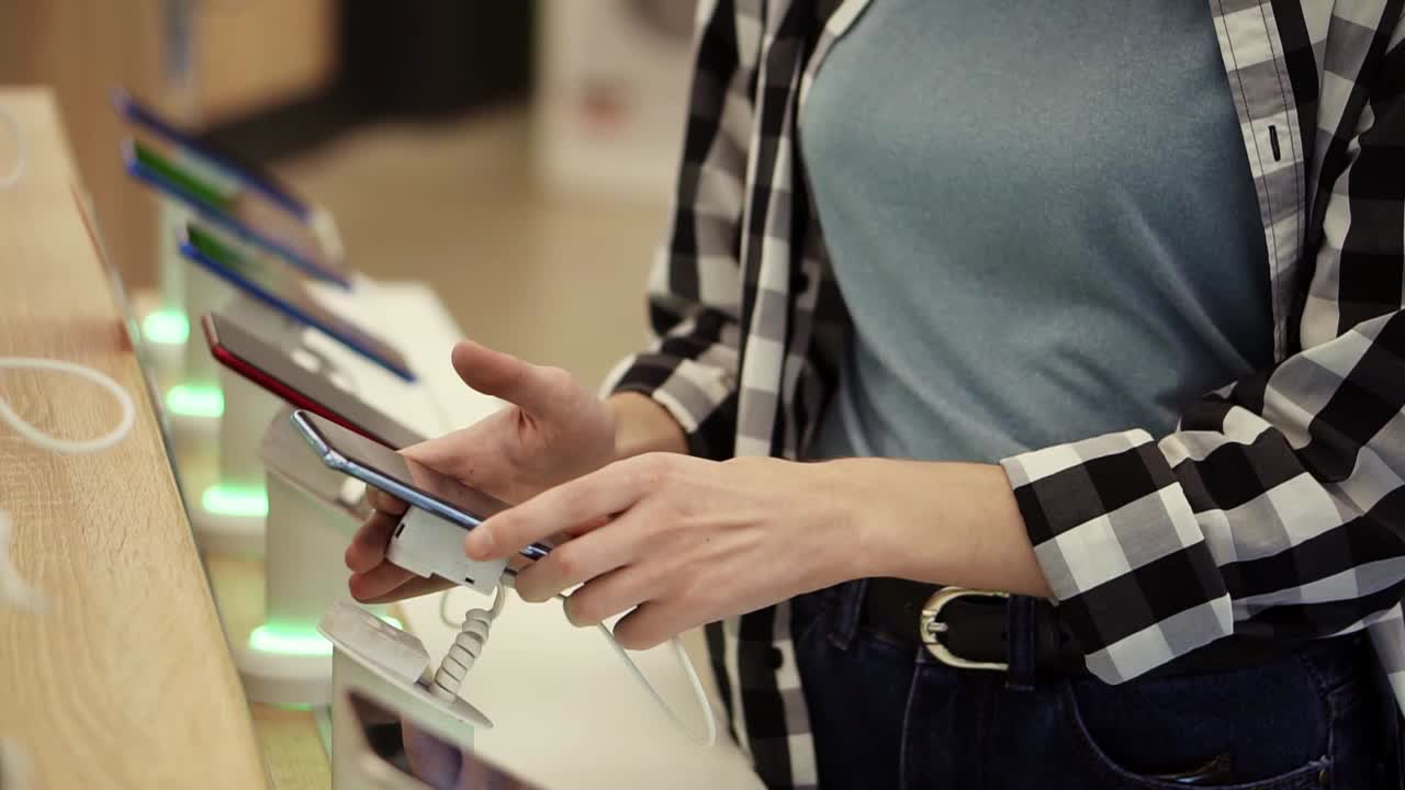Waist shot of unrecognizable woman's hands chooses a smartphone in and electronics store. She takes smartphone from counter and