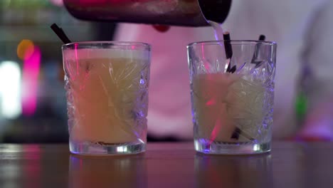 Tropical-yellow-cocktail-poured-from-stainless-steel-shaker-into-glass-with-black-straw