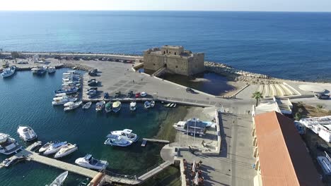 toma aérea alejándose del castillo de pafos tierra adentro, mostrando muelles para botes y corredores corriendo por el puerto.