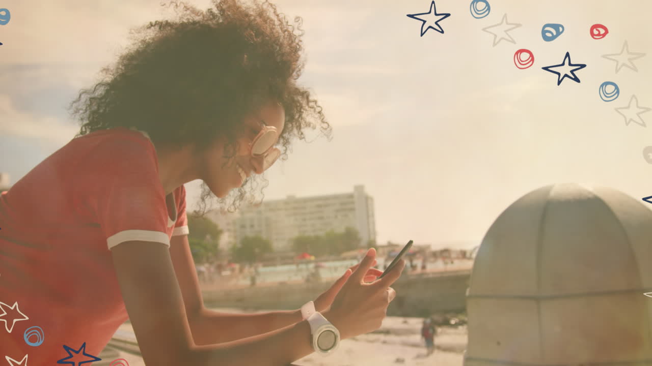 Colorful star icons against african american woman using smartphone near the beach