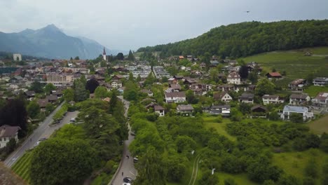 dolly aéreo fuera del pintoresco valle verde de spiez y pueblo que revela el castillo medieval, el bosque y los alpes suizos en segundo plano.