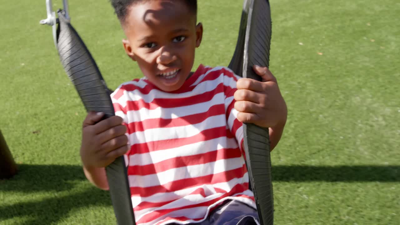 Front view of African American schoolboy playing on a swing in school playground 4k