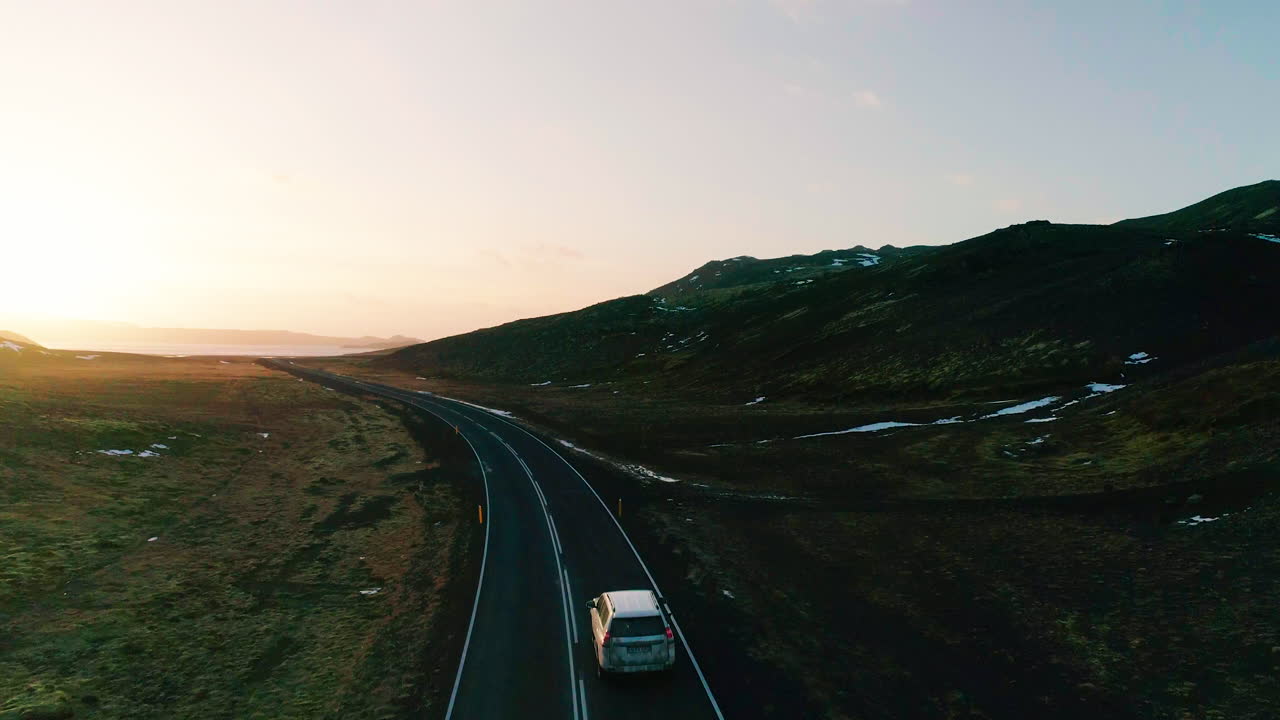 Kleifarvatn luftfoto, der følger et køretøj på en lang vej mod tågede solnedgangsbakker