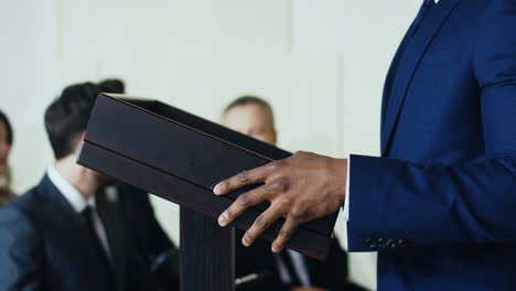 close-up view of african american male hands on a podium while businesswoman is making a speech to the audience at a conference