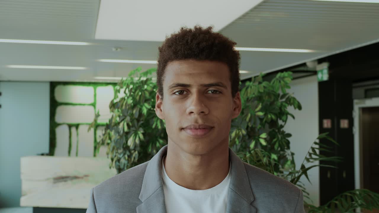hombre negro guapo en traje. joven hombre afroamericano en traje elegante de pie en una oficina moderna y sonriendo felizmente a la cámara
