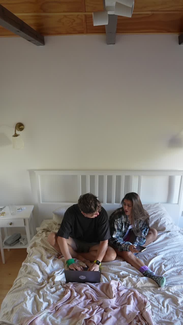 una pareja relajándose en la cama con una computadora portátil y un teléfono