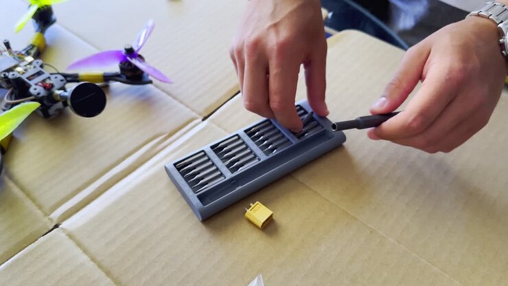Hands search for specialized screwdriver head as they fix and repair a FPV drone