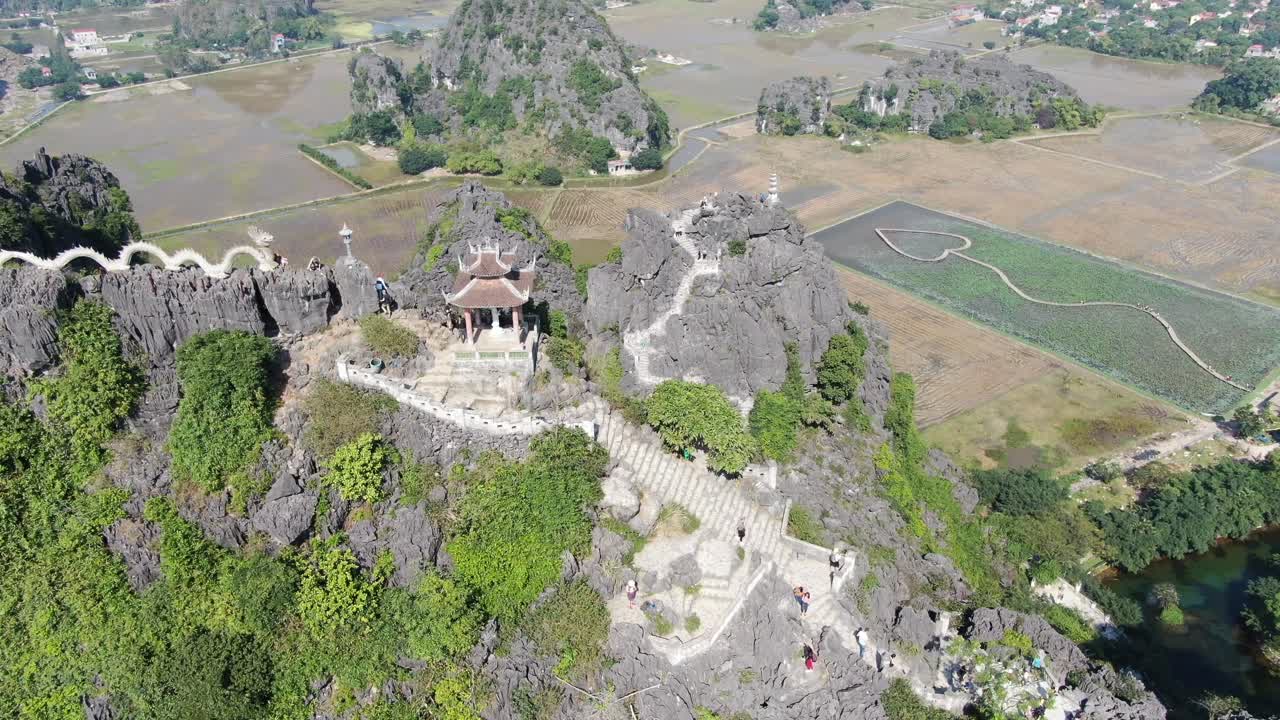 drone vista aérea en vietnam volando hacia abajo en frente de la montaña rocosa cubierta de árboles verdes con escaleras y un templo en ninh binh en un día soleado