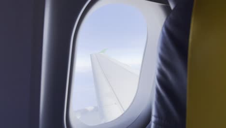 wing of an airplane seen through the window from a passenger seat in the middle of the sky