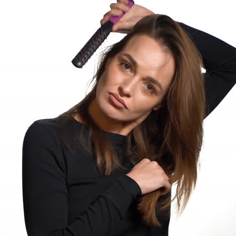 a pensive woman with long hair is looking straight and parallelly combing her hair on a white background. close-up.