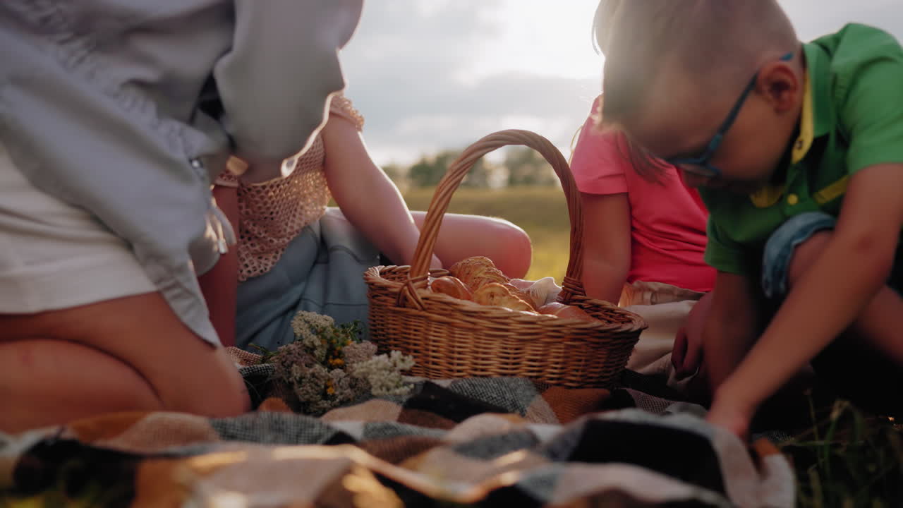 쾌적한 가족이 야외에서 피크닉을 즐기고 있는 클로즈업, 은 빛이 황금색 빛을 더하는 동안 과 간식으로 가득 찬 바구니가 직물 위에 앉아 있습니다.