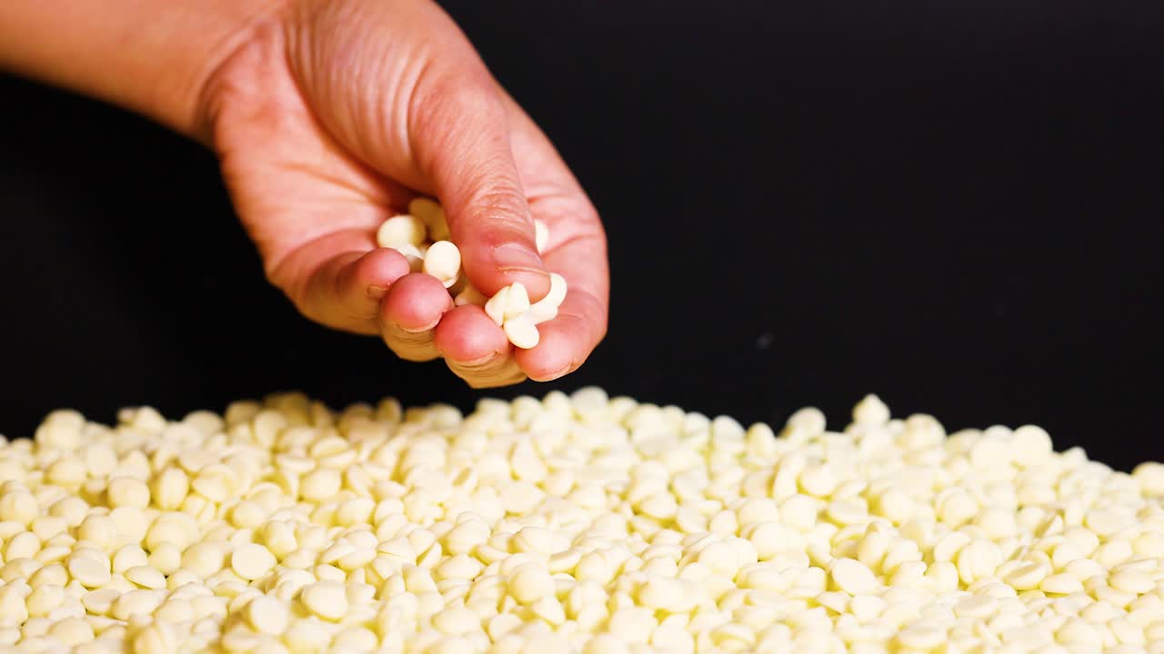 Hand scooping white chocolate chips from pile