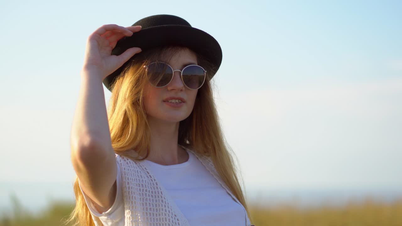 женщина в поле с шляпой и солнцезащитными очками