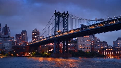 Train moves by the Manhattan Bridge. View on the bridge from the waterscape. Skyline of New York under cloudy sky at backdrop