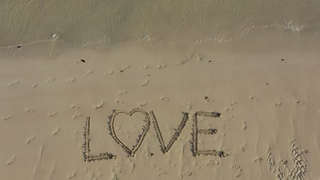 love inscribed in the sand on a beach and fills the frame and gets smaller in time