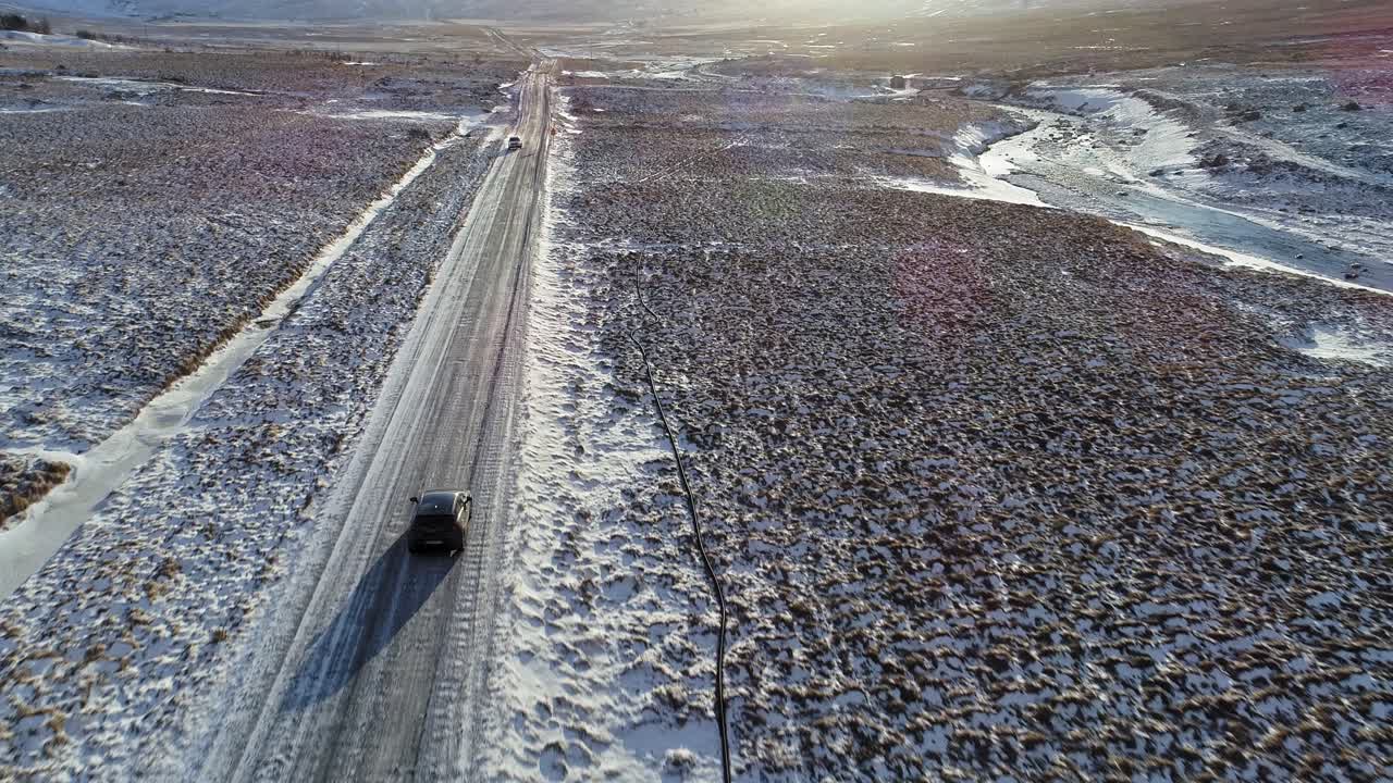 camiones conduciendo por la carretera asfaltada rodeada de campos nevados en islandia con montañas escénicas y sol brillante en el fondo - toma aérea de drones